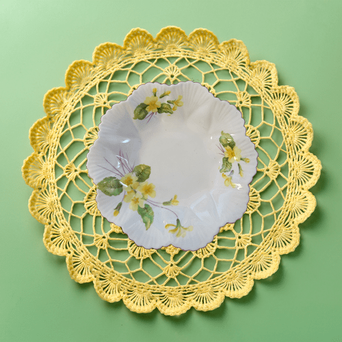 Decorative yellow lace doily with a floral plate on a green background