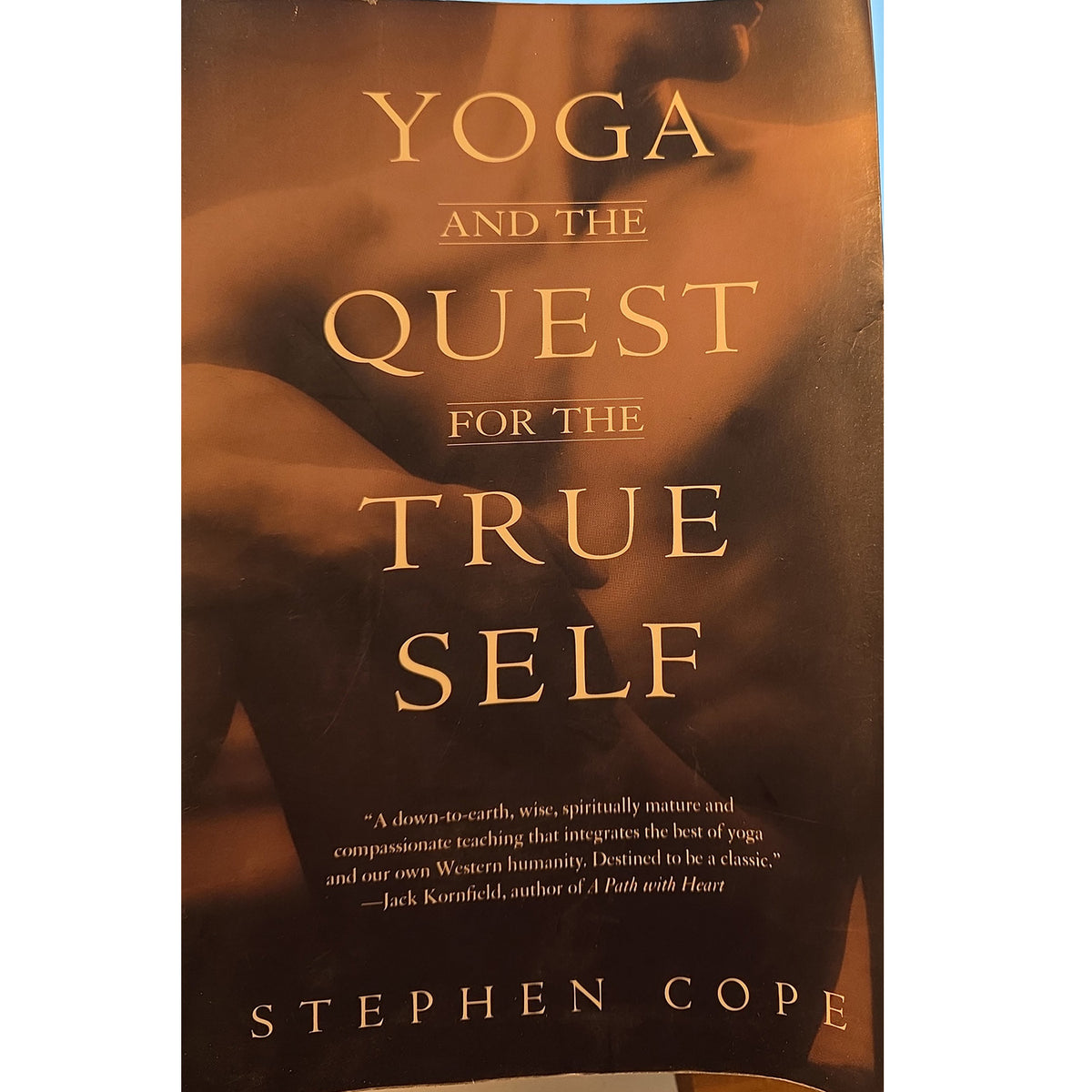 Book cover of 'Yoga and the Quest for the True Self' by Stephen Cope, featuring a warm brown and gold-toned design with a blurred figure in the background and gold lettering.